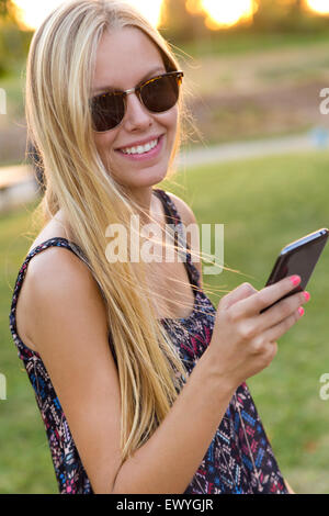 Outdoor portrait of young beautiful girl texting avec son téléphone. Banque D'Images