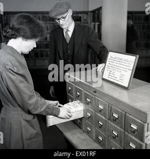 Historique, 1950, jeunes femmes à la bibliothécaire dans l'index de la carte système de dépôt pour aider un homme âgé dans une bibliothèque. Banque D'Images