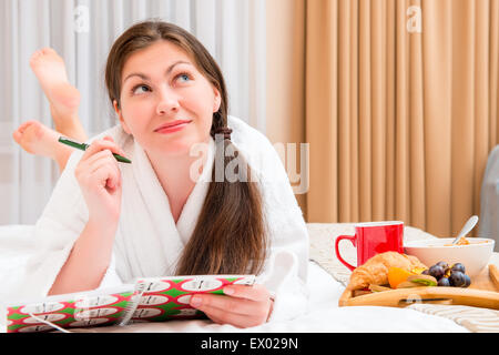 Jeune femme avec un ordinateur portable et un petit déjeuner au lit Banque D'Images