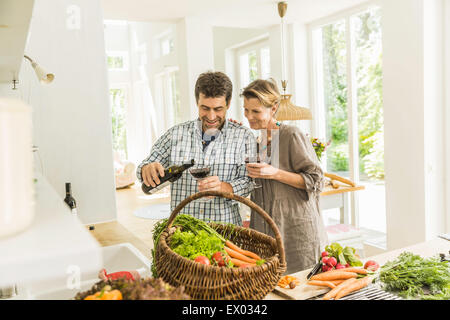 Couple pouring red wine tout en préparant des légumes frais Banque D'Images