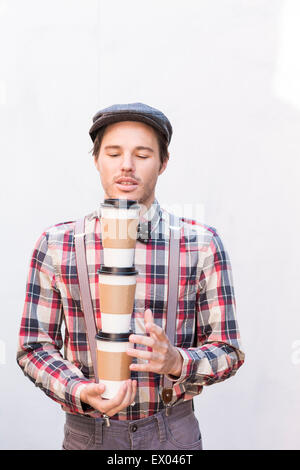 Jeune homme avec les yeux fermé portant trois cafés à emporter Banque D'Images