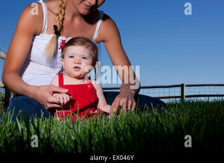 Portrait of mid adult woman sitting on grass avec enfant fille Banque D'Images