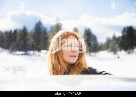 Portrait of mid adult woman gazing sur toit de voiture dans un paysage couvert de neige Banque D'Images