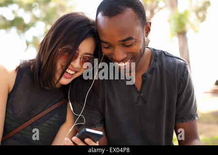 Jeune couple assis ensemble, partageant les écouteurs Banque D'Images