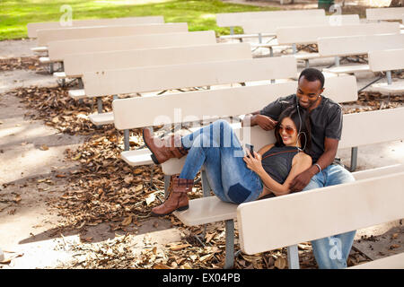 Jeune couple assis sur un banc, le partage d'écouteurs Banque D'Images