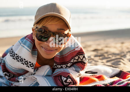 Portrait de jeune femme assise sur la plage, le port de lunettes de soleil et chapeau Banque D'Images