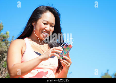 Mid adult woman en vêtements de sport, le port d'écouteurs, holding smartphone Banque D'Images