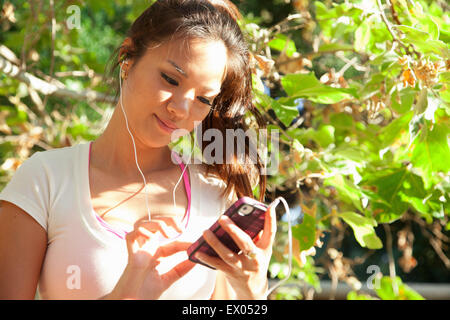 MId adult woman wearing earphones et holding smartphone, à l'extérieur Banque D'Images