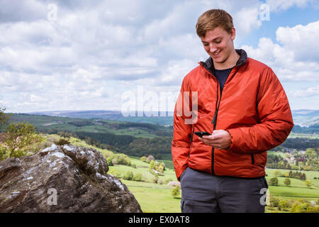 Teenage Male hiker reading textes sur smartphone haut de Guise, Falaise, Campsites Canet-en-Roussillon Nidderdale, Yorkshire Dales Banque D'Images