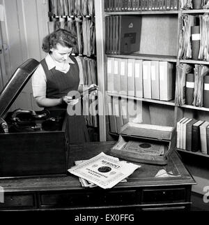 Historique, 1950, photo montre une jeune femme dans la sélection de musique d'une bibliothèque choisissez un disque vinyle à jouer sur le gramophone machine. Banque D'Images