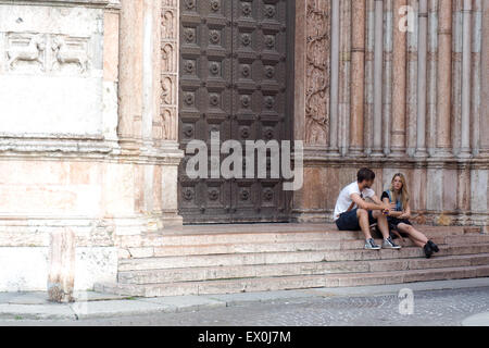 Un jeune couple assis sur les marches à l'entrée du baptistère de la cathédrale de Parme, Banque D'Images