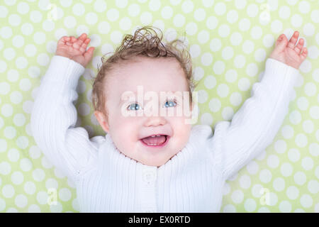 Funny rire happy baby avec de beaux yeux bleus et des cheveux bouclés à jouer sur une couverture verte portant chandail tricoté blanc chaud Banque D'Images