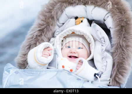 Happy laughing baby girl bénéficiant d'une promenade dans un parc d'hiver enneigés assis dans une poussette avec capot de mouton Banque D'Images