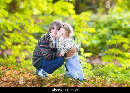 Cute frère et sa petite sœur serrant et jouer ensemble dans un magnifique parc ensoleillée d'automne Banque D'Images