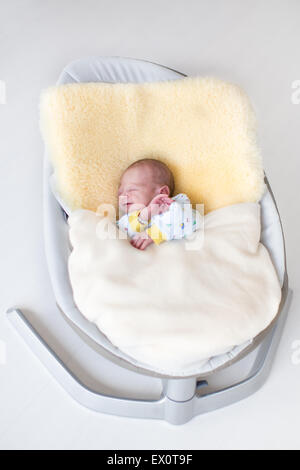 Sweet bébé nouveau-né garçon endormi dans un swing sur un mouton sous une couverture en tricot chaud Banque D'Images