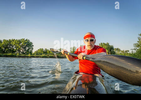 Senior male paddler formation dans une course en kayak de mer, avec une aile pagayer sur un lac, de flou de paddle Banque D'Images