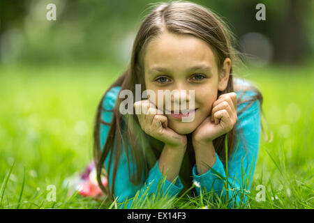 Close-up portrait of a neuf ans, fille, couché dans l'herbe verte. Banque D'Images