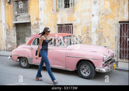 La HAVANE, CUBA - 13 juin, 2011 : Jeune Cubaine femme marche à côté vintage American voiture de taxi en face de bâtiments coloniaux altérés. Banque D'Images