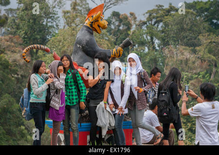 Filles d'âge scolaire ayant une séance de photo devant une statue de personnage de tigre à Padar Alam, Sumatra Sud, Indonésie. Banque D'Images