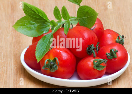 La tomate (Solanum lycopersicum) et le basilic dans un plat blanc sur fond de bois Banque D'Images