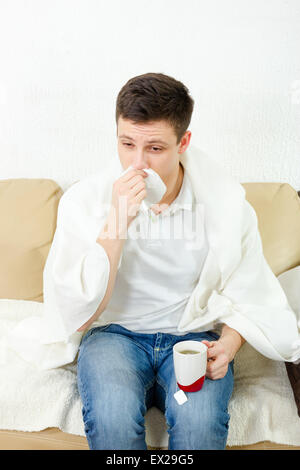 Jeune adulte homme malade de sentiment. Modèle masculin ayant froid intense. Les éternuements et nez de nettoyage avec le papier de soie en maintenant tasse de Banque D'Images