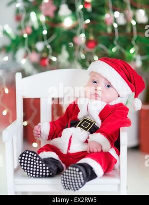 Mignon bébé nouveau-né garçon dans un Santa outfit assis sous un Noël blanc décoré dans un fauteuil à bascule Banque D'Images