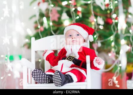 Peu de nouveau-né baby boy in Santa outfit assis sous un arbre de Noël Banque D'Images