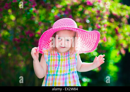 Petite fille mignonne avec des fleurs. Enfant portant un chapeau rose jouant dans un jardin d'été. Jardinage pour les enfants. Banque D'Images