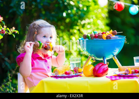 Les enfants de la viande cuisson. Camping en famille et profiter du barbecue. Petite fille à préparer un barbecue biftecks, brochettes et le maïs. Banque D'Images