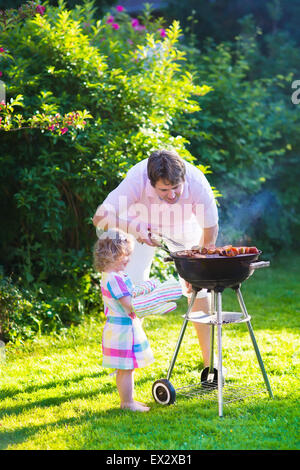 Le père et l'enfant la cuisson de la viande. Camping en famille et profiter du barbecue. Père et fille au barbecue préparation des steaks et des saucisses. Banque D'Images