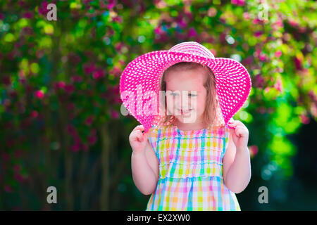 Petite fille mignonne avec des fleurs. Enfant portant un chapeau rose jouant dans un jardin d'été. Jardinage pour les enfants. Les enfants jouent la surenchère Banque D'Images