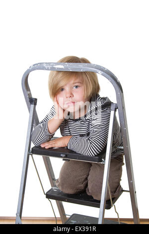 Jeune garçon portant chemise rayée et le capot, assis sur une échelle, souriant à la caméra. Banque D'Images