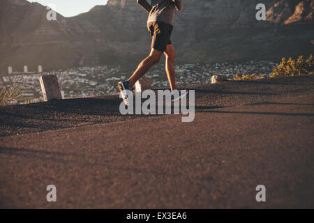 La section basse image de jeune homme en marche sur route de campagne et matin. L'accent sur les jambes de l'athlète masculin. Banque D'Images