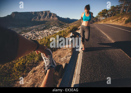 Shot POV de l'homme étend sa jambe avec femme l'exercice par une route garde-corps. Les jeunes se détendre leurs muscles après matin Banque D'Images