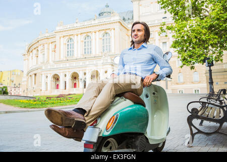 Beau jeune homme se reposant sur un scooter dans la vieille ville d'Europe Banque D'Images