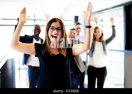 Jeune femme blanche directrice debout devant des collègues avec leurs bras levés. Banque D'Images