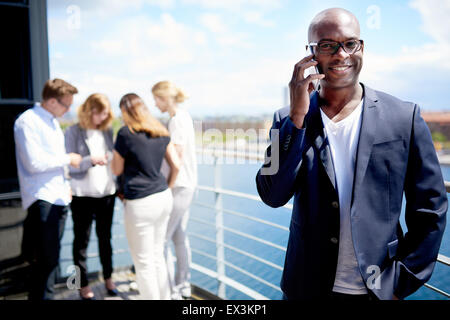 Black male executive smiling holding portable à l'oreille et l'article avec la main dans la poche Banque D'Images