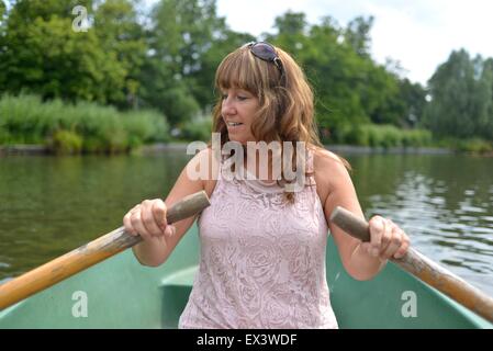 Femme attirante avirant un bateau sur un lac de canotage pendant portant une robe d'été Banque D'Images