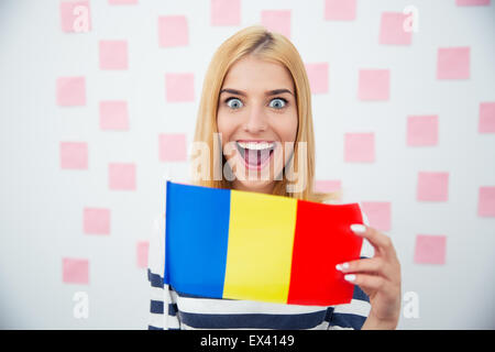 Cheerful young woman holding drapeau roumain avec des autocollants sur l'arrière-plan. Looking at camera Banque D'Images