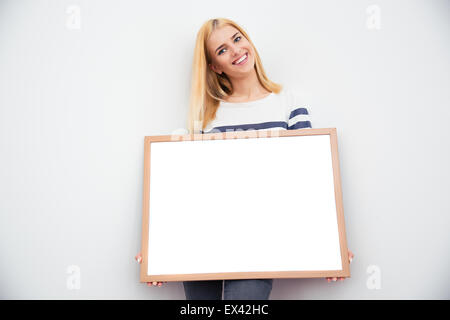 Young casual businesswoman holding blank board sur fond gris Banque D'Images