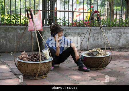 Hanoi Vietnam femme vend des marrons tout en parlant sur son téléphone portable à l'extérieur du Temple de la littérature Banque D'Images