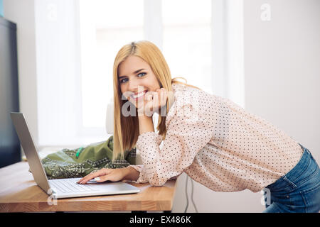 Smiling Fashion designer using laptop and looking at camera in workshop Banque D'Images