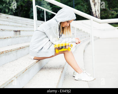 Assez jeune fille assise sur l'escalier avec skateboard Banque D'Images