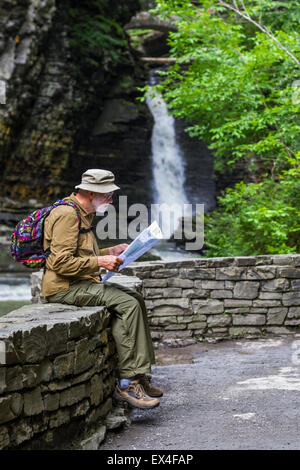 Un homme regarde une carte des pistes avec une cascade en arrière-plan, à Watkins Glen State Park, New York Banque D'Images