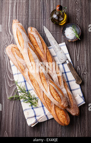 Trois Baguette française fraîche, huile d'olive extra vierge et de romarin sur fond de bois gris Banque D'Images