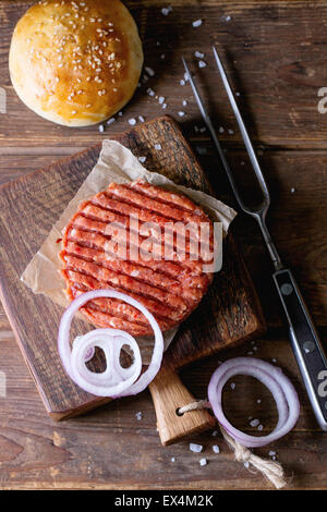 Escalope de matières premières, frais et oignons pain de traitement au four pour faire des hamburger, servi sur la petite planche à découper en bois avec o fourchette à viande Banque D'Images