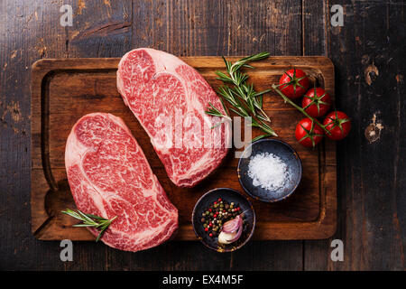 Deux matières produits frais Viande marbrée Black Angus Steak Ribeye et les assaisonnements sur fond de bois foncé Banque D'Images