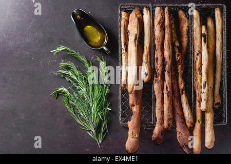 Des petits pains bâtons grissini maison vintage en métal fort à l'huile d'olive et des herbes de romarin et thym sur tensioactifs sombre Banque D'Images