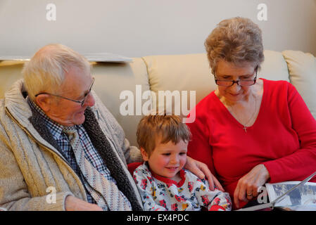 Un tout-petit (3 ans) en pyjama ayant une histoire avec ses grands-parents Banque D'Images