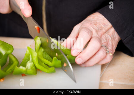 Woman chopping de poivrons verts sur une planche à découper en plastique en préparation pour faire plaisir Banque D'Images